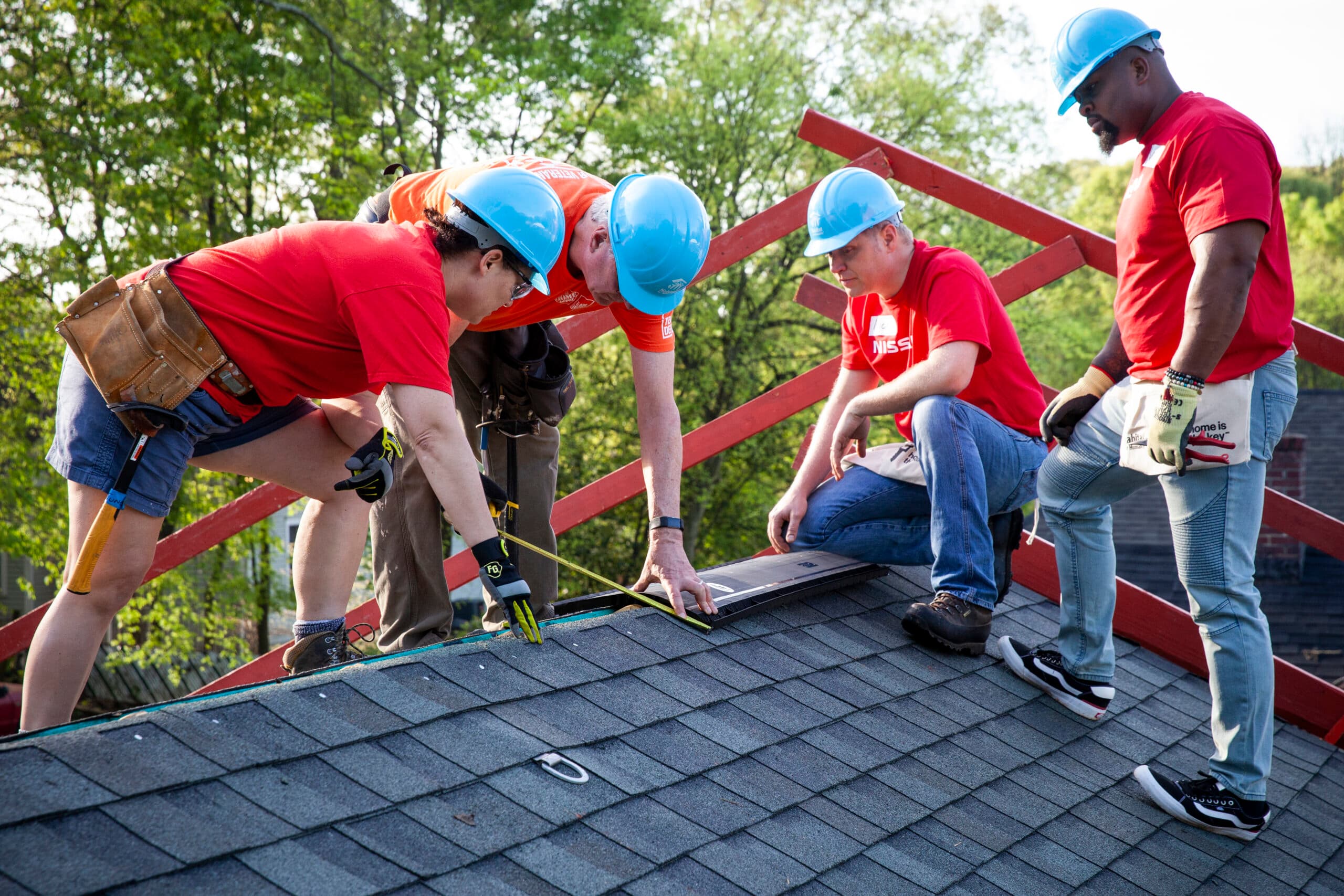 Volunteers in red shirts measuring and installing roof decking on a Habitat build site